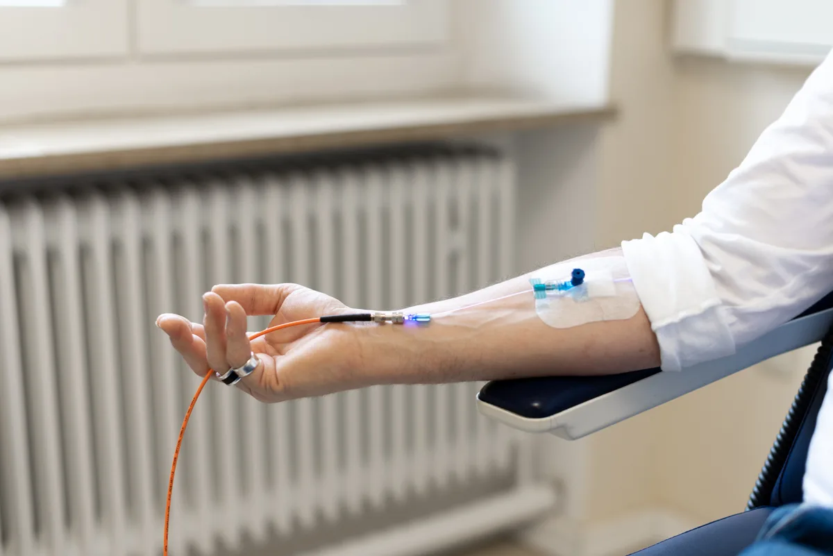 A thin blue-lit fibre connected to a cannula taped to a forearm